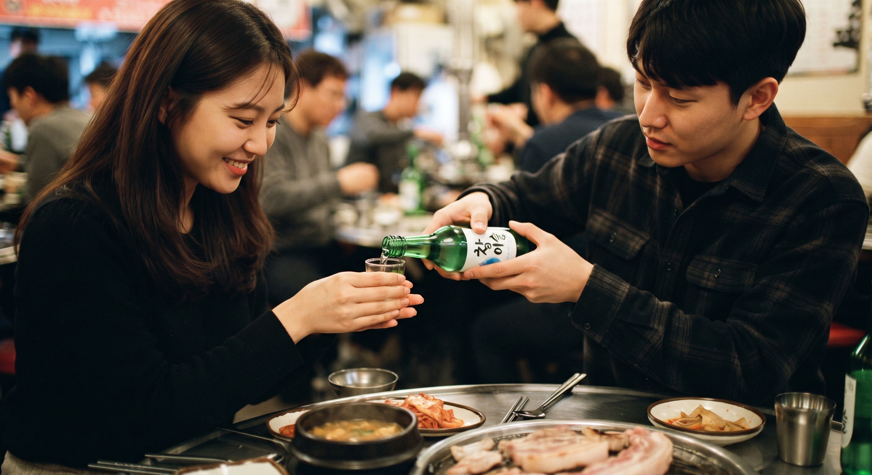 Hands pouring soju into small glasses at a Korean dinner table